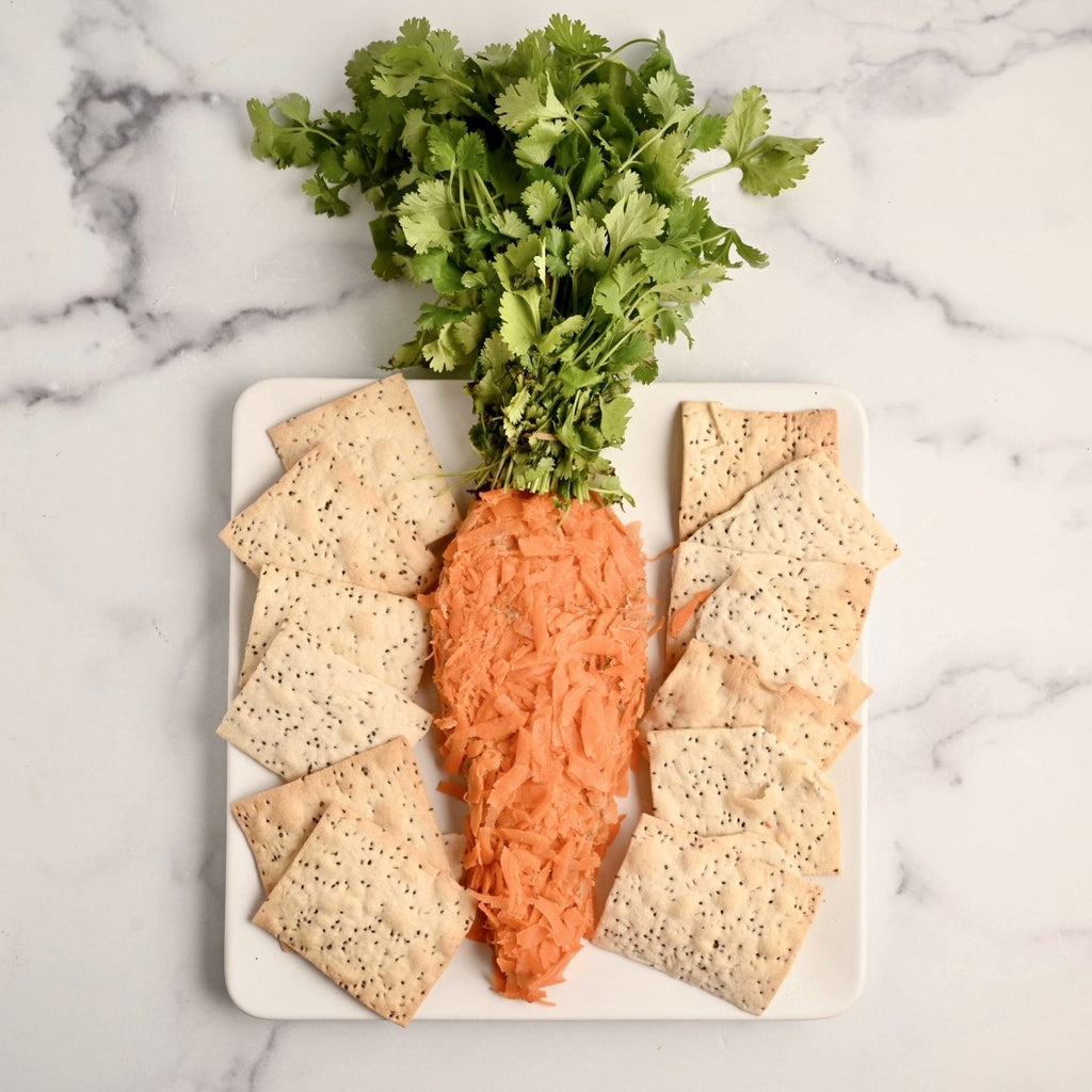 White ceramic plate covered in crackers and a giant homemade carrot shaped spread