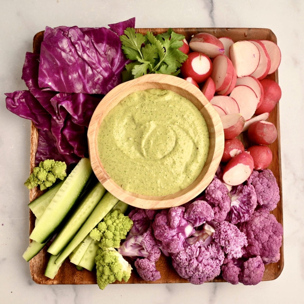 Cutting board covered in fresh vegetables with a bowl of green dipping sauce in the middle