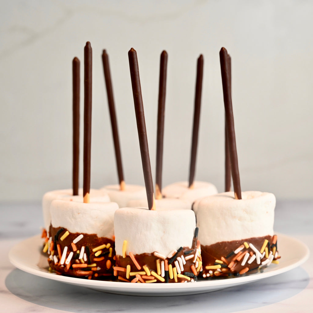A plate of marshmallows dipped in chocolate with Halloween sprinkles