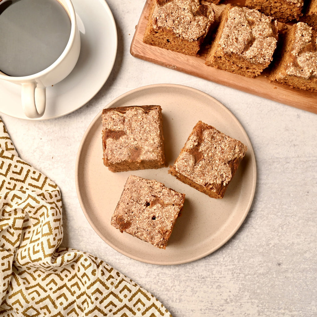 A plate of three slices of pumpkin coffee cake with a mug of coffee next to it