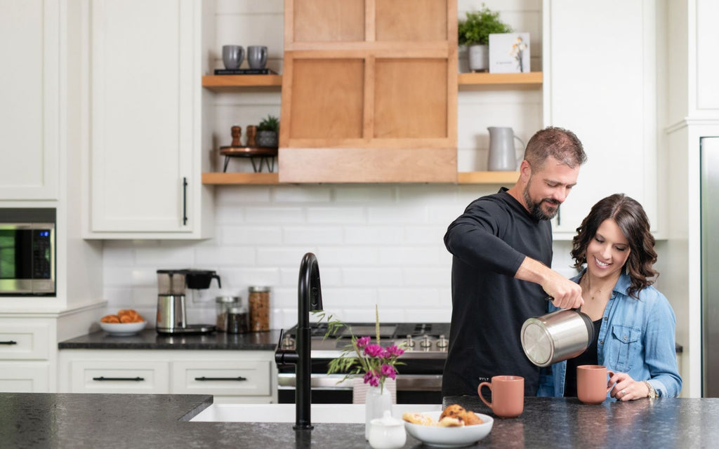 A man is pouring coffee from a carafe into a mug for a woman.