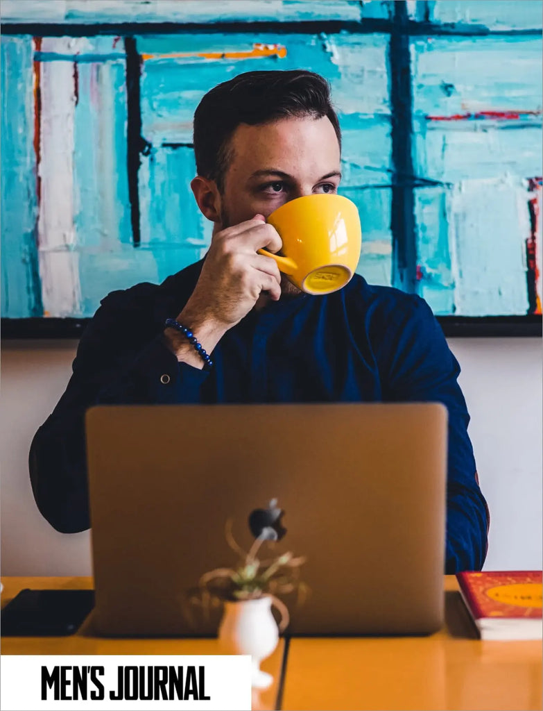 Man working on a computer whilst drinking a coffee.
