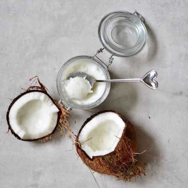 A coconut split into two on a white marble kitchen counter. Next to the coconut is a jar containing coconut oil..