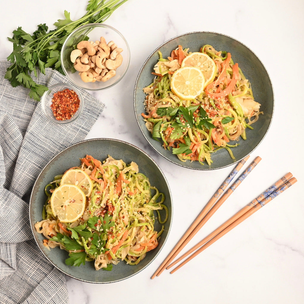 A grey kitchen towel is wrapped over a kitchen counter with two grey bowls full of homemade vegetable stir fry with a set of chopsticks resting nearby