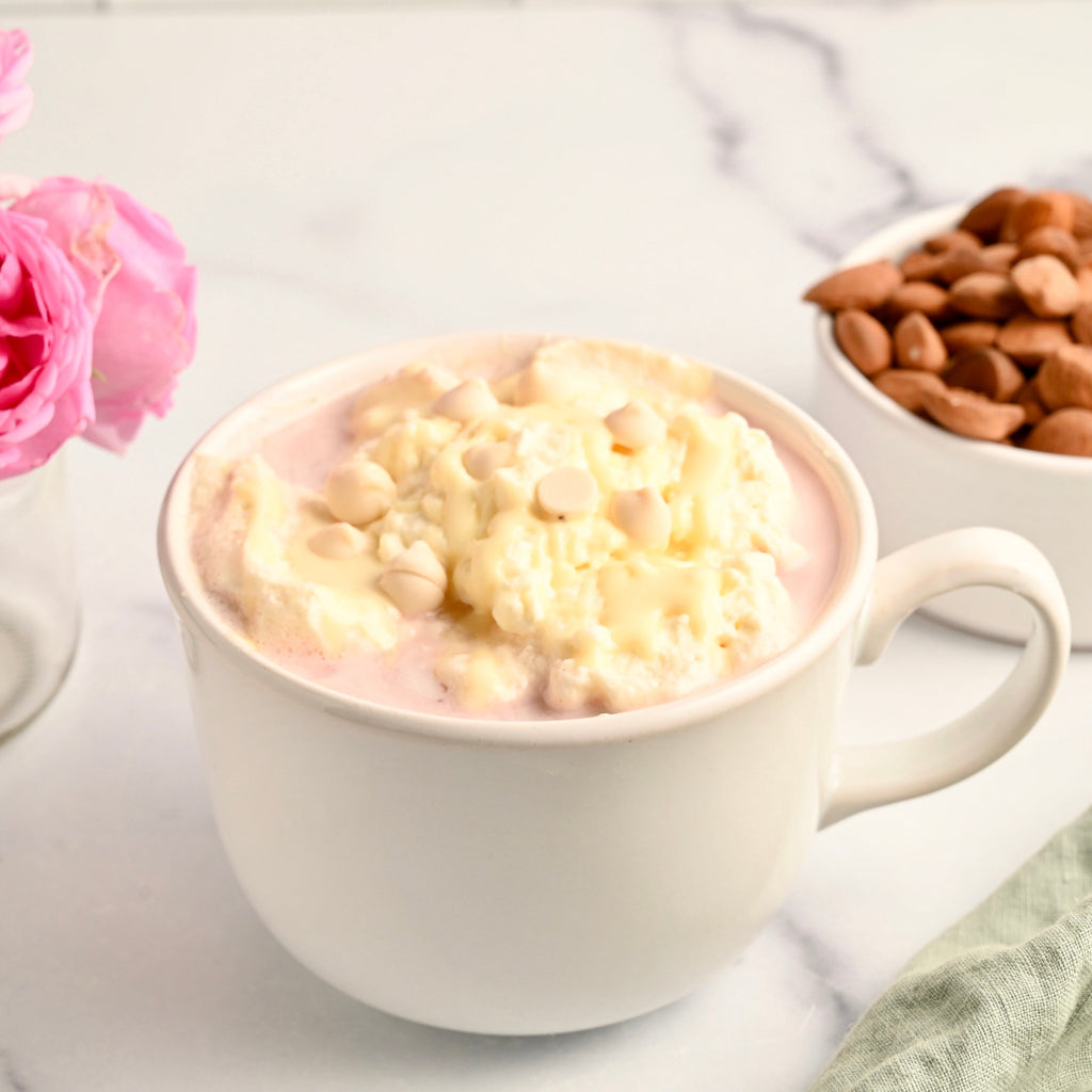 A white ceramic coffee mug is filled with a pink hot chocolate beverage and topped with melted white marshmallows