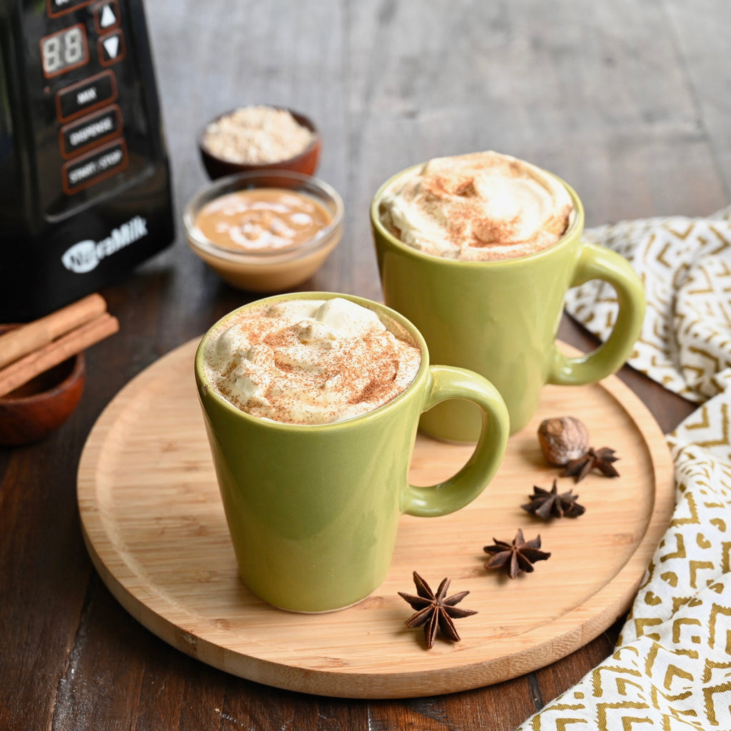 A wooden tray contains two light green mugs both filled with gingerbread lattes and topped with frothy whipped cream
