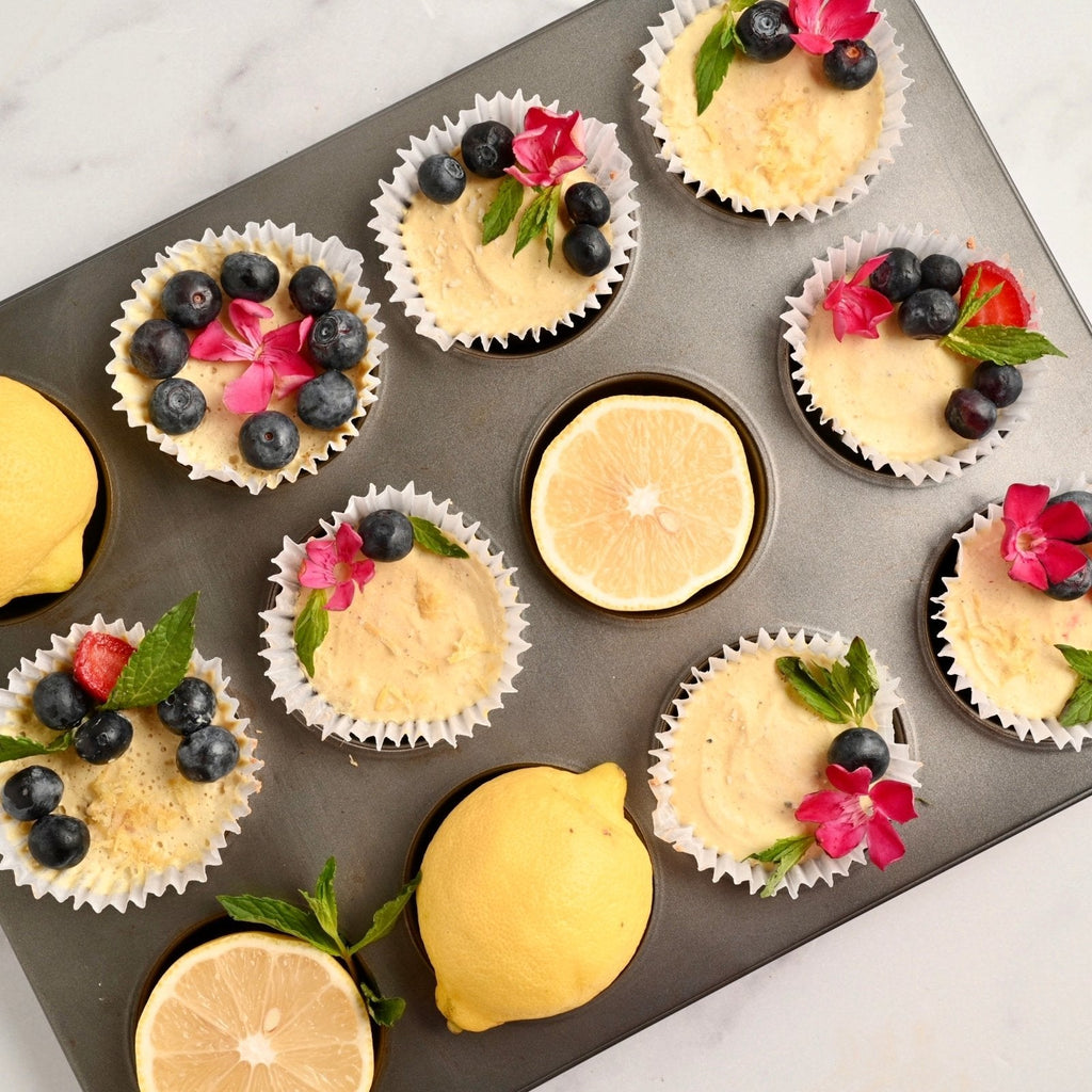 Muffin tin filled with individual lemon tarts each topped with fresh fruit and flowers