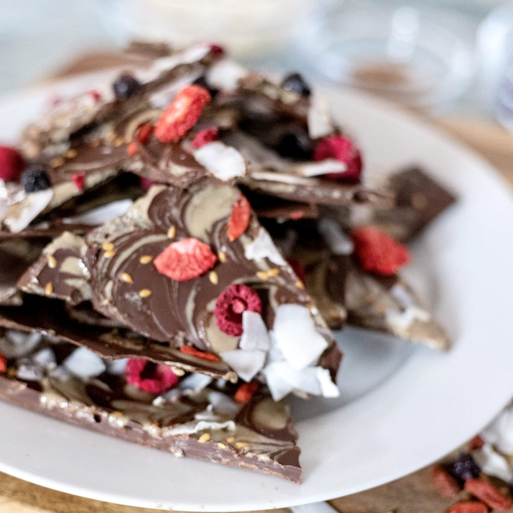 White ceramic plate with large pieces of milk chocolate bark topped with white coconut flakes and bright red dried berries