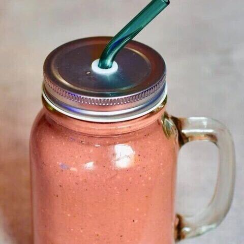 Clear plastic glass filled with a pink smoothie and a blue straw
