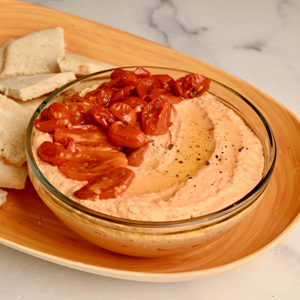 A wooden cutting board with a glass dish filled with homemade hummus