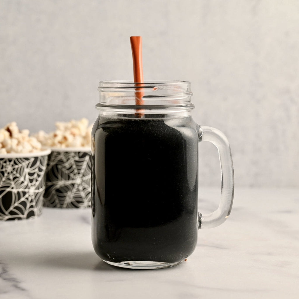 Clear mason jar glass filled with a black colored smoothie with an orange straw