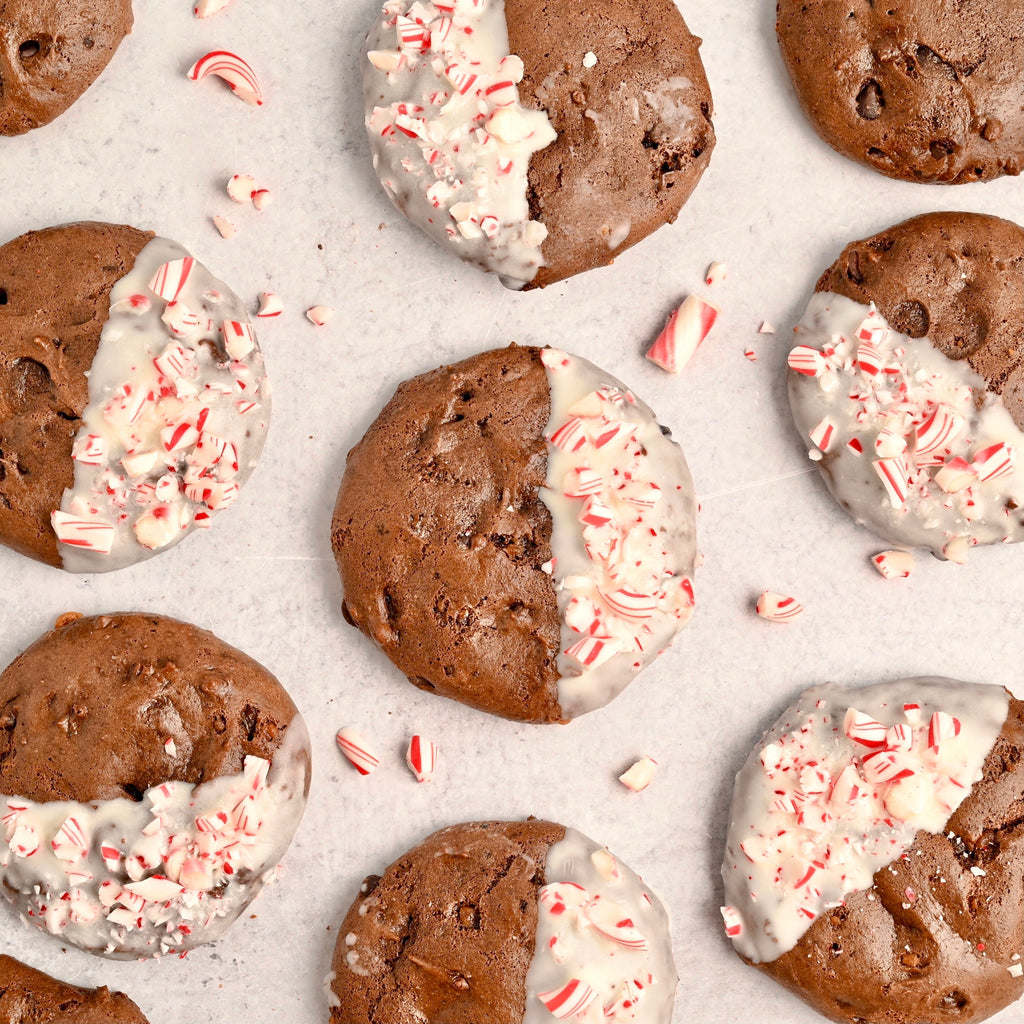 White parchment paper is adorned in chocolate cookies that have been dipped in white chocolate and covered in crushed candy canes