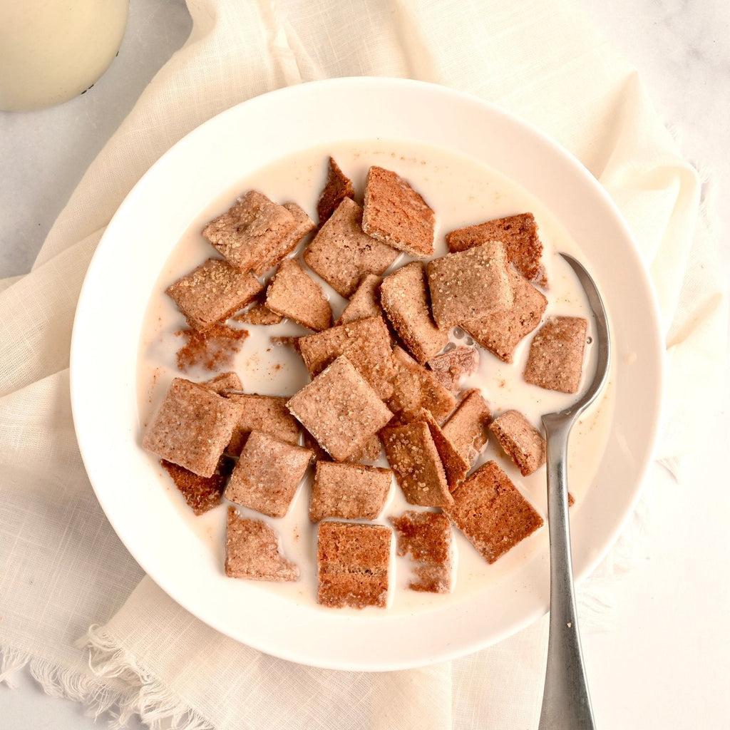 A white ceramic bowl filled with homemade Cinnamon Toast Crunch cereal and milk with a spoon off to the side