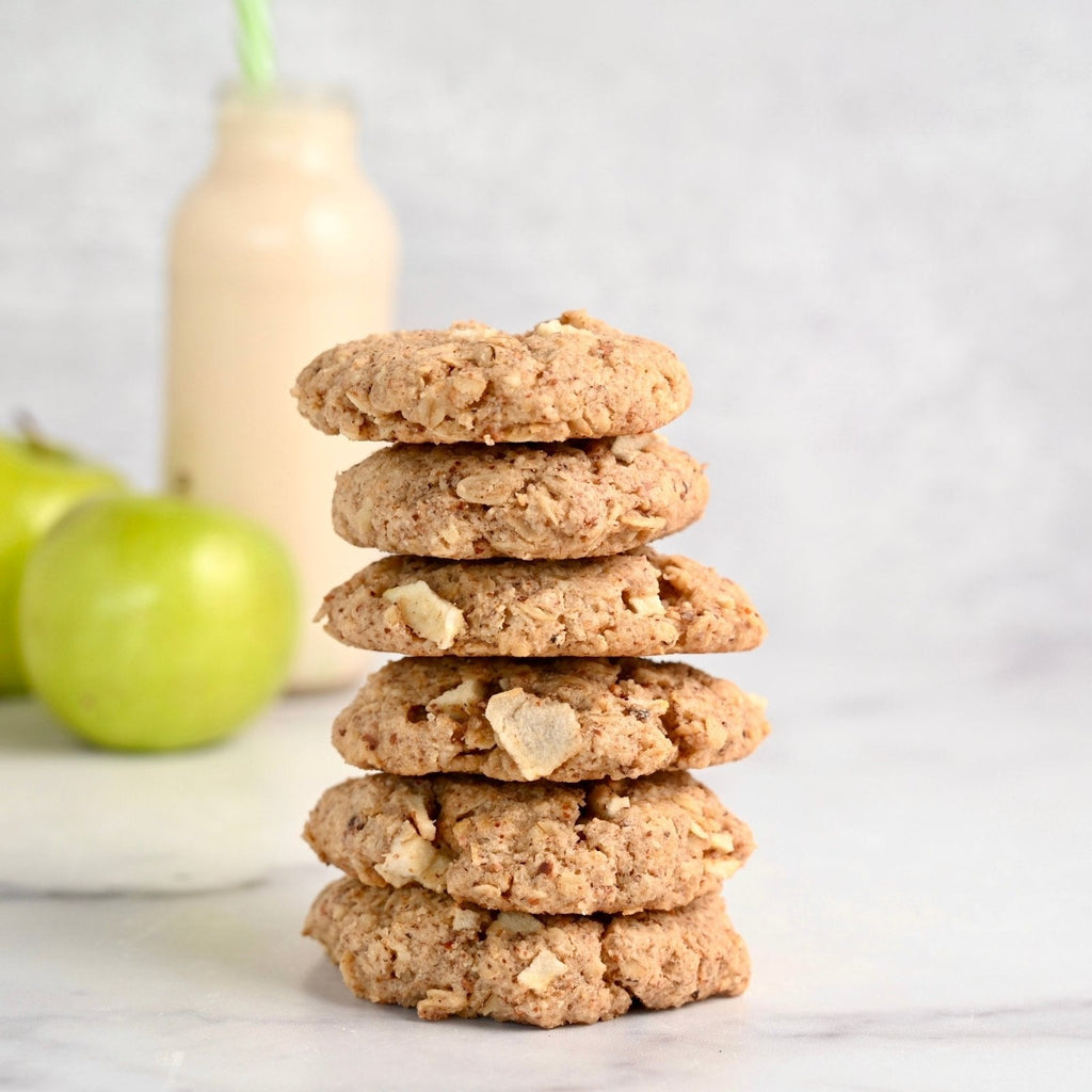 A stack of apple oatmeal cookies with a green apple and a glass pitcher of milk in the background