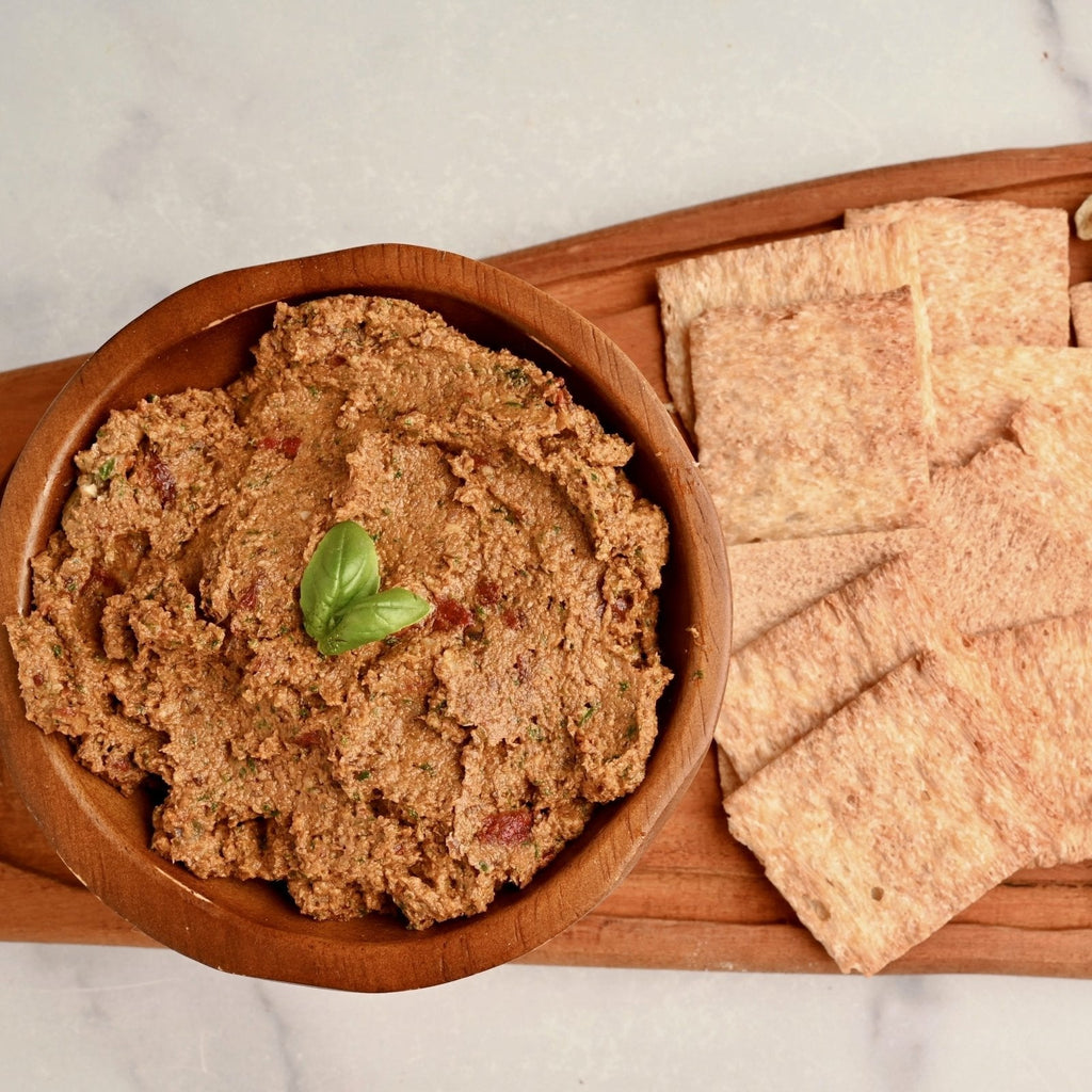 Wooden cutting board with a bowl of olive tapenade and crackers