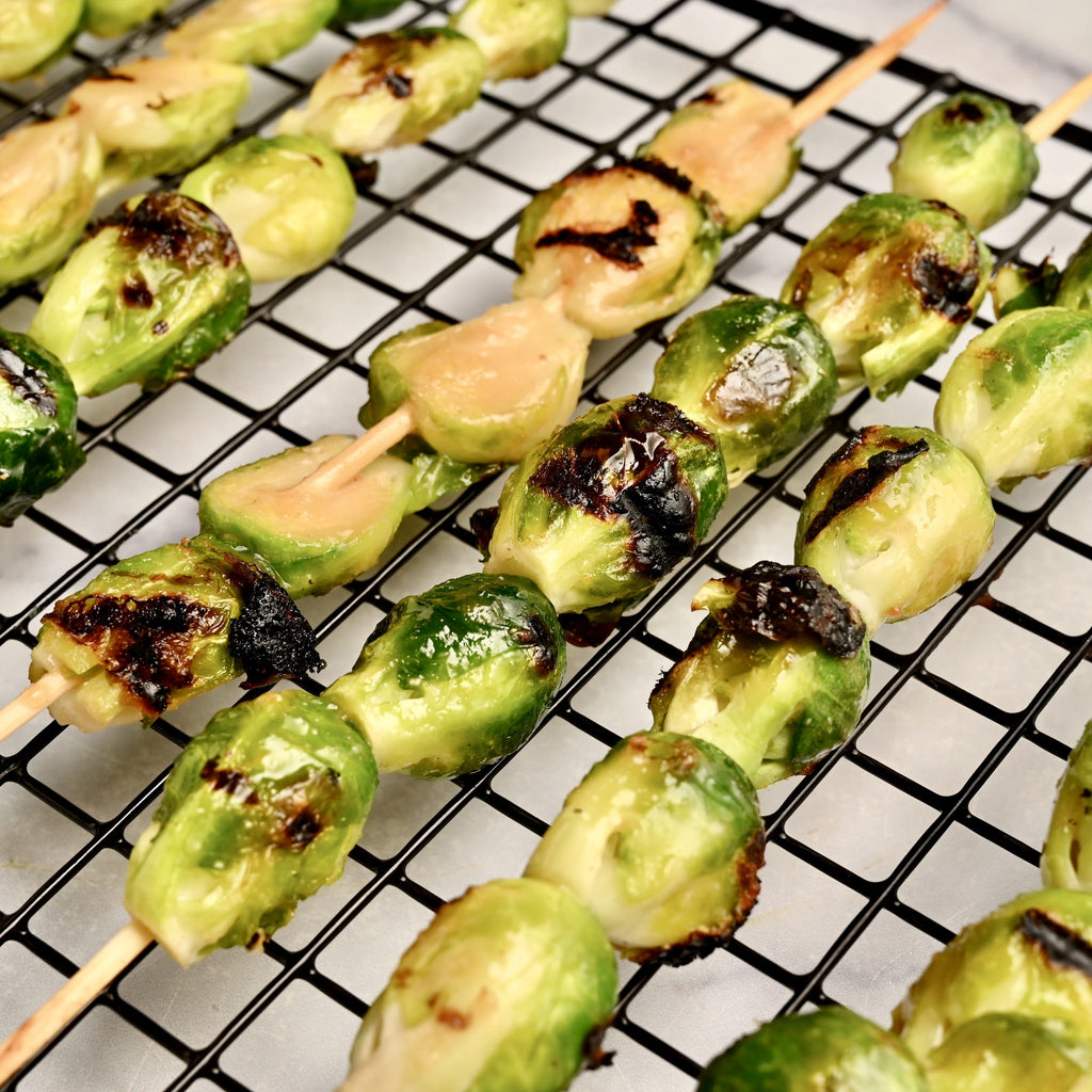 Rows of grilled Brussels sprouts on skewers and topped with a creamy peanut sauce