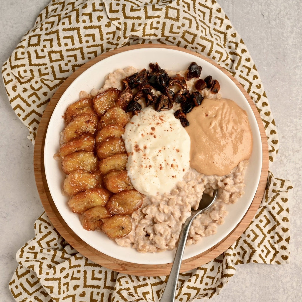 A bowl of oatmeal topped with caramelized bananas, cinnamon, dates, nut butter and yogurt