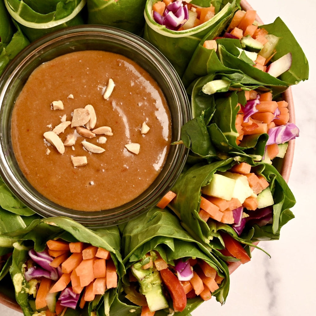 Collard greens packed with fresh vegetables surrounding a bowl of homemade peanut sauce