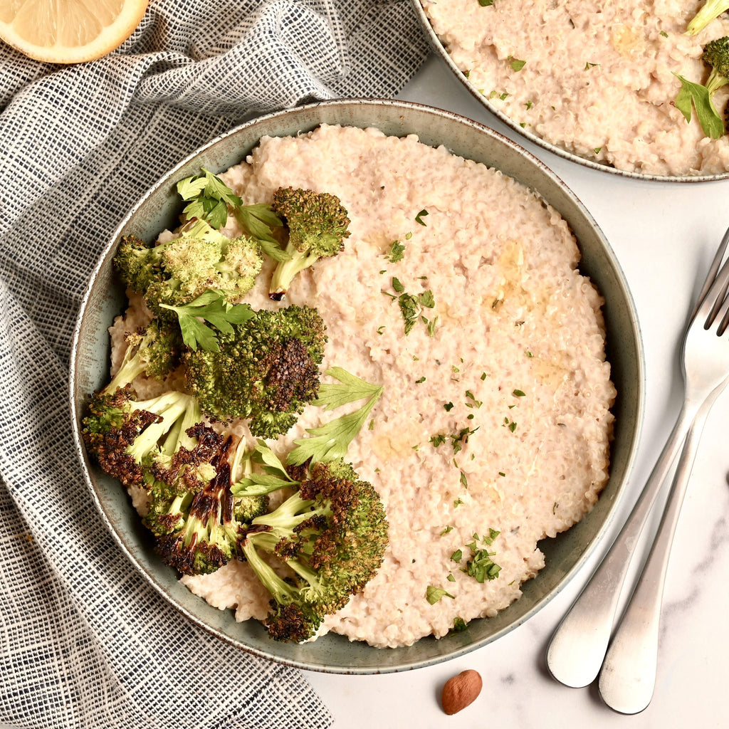 Grey bowl with quinoa risotto and fresh broccoli florets with a fork and knife to the right of the bowl