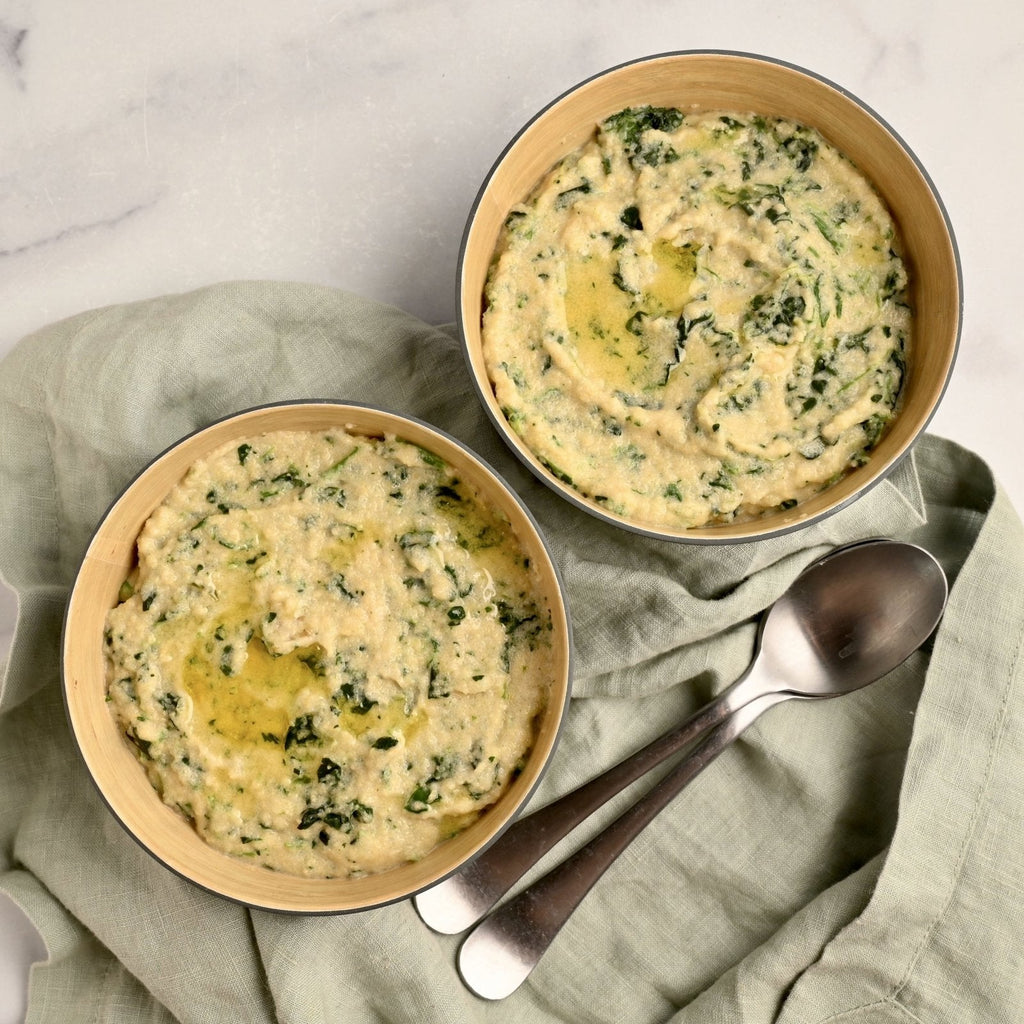Two bowls with creamy spinach polenta and spoons off to the side