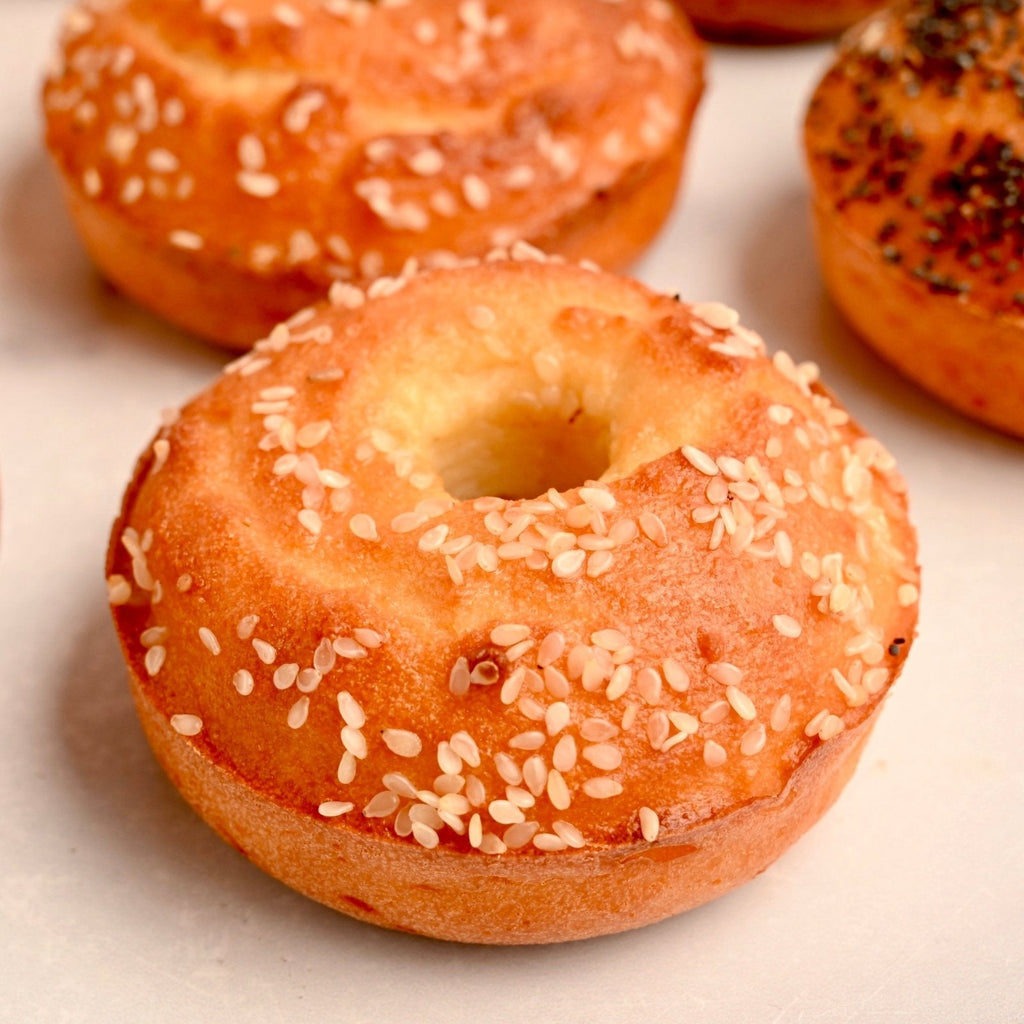 A white plate with homemade toasted bagel with sesame seeds on top