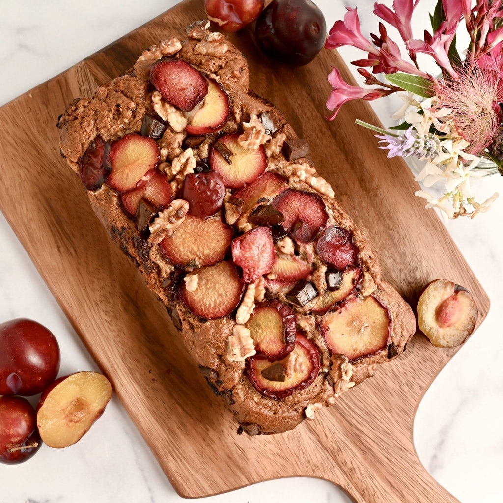 Brown cutting board with a loaf of bread covered in fresh plum slices