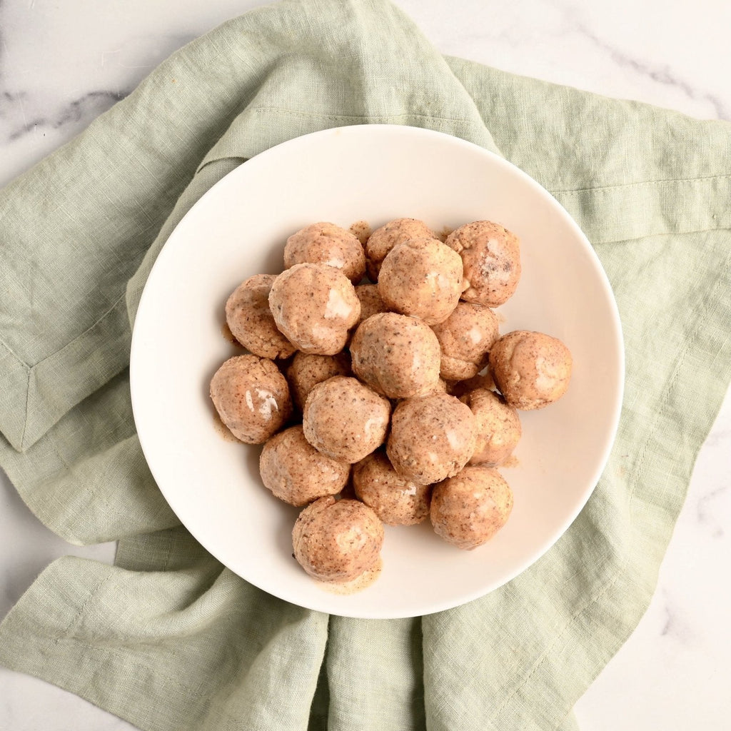 A light green kitchen towel with a white ceramic plate on top stacked with a pile of keto donut holes
