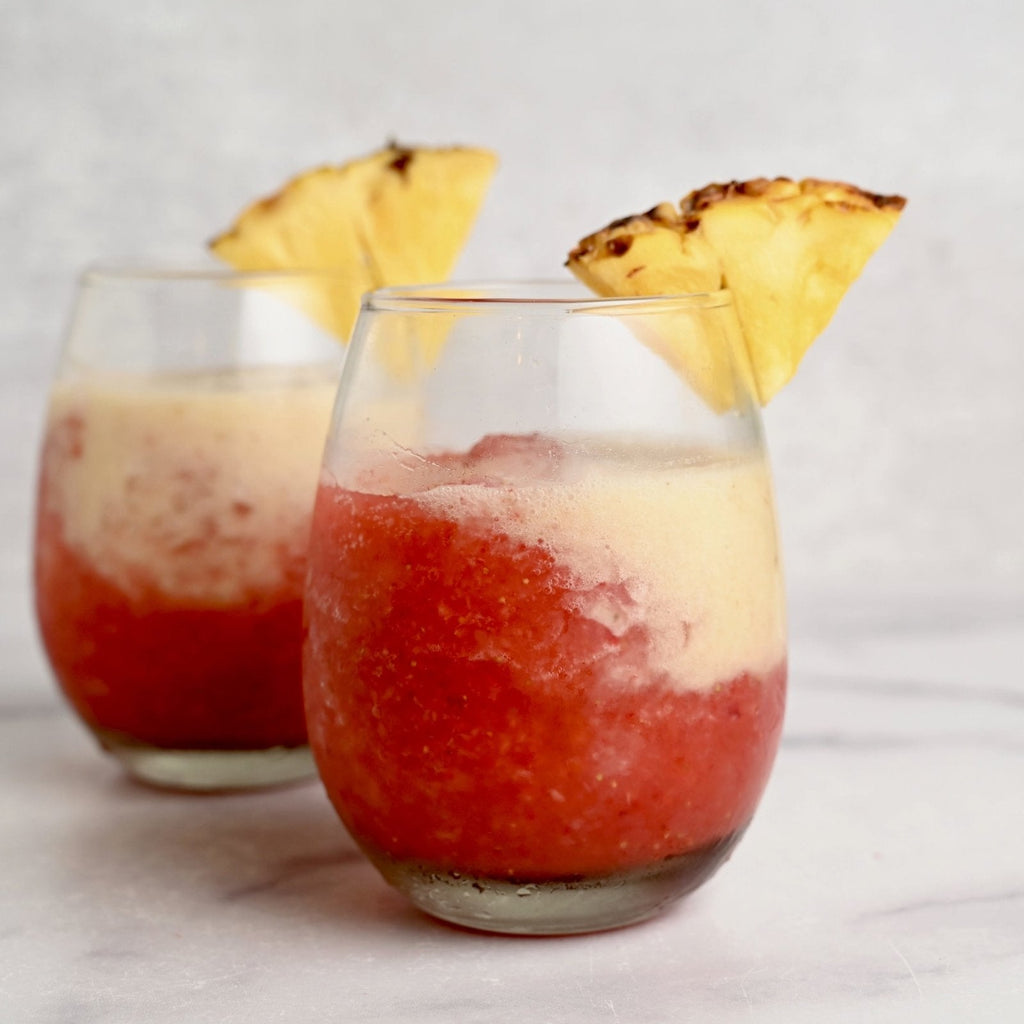 Two glass cups filled with a red fruity drink and pineapple slices on the rim of each glass