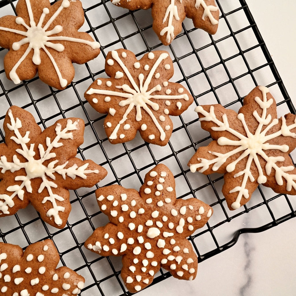 Gingerbread cookies in the shape of snowflakes with white icing cooling on a cooling rack