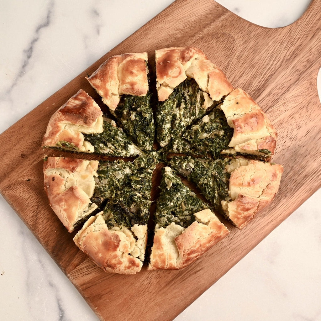 A brown wooden cutting board with a spinach and mushroom galette in the center