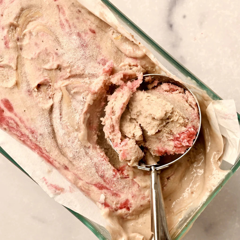 A clear serving dish filled with peanut butter and berry ice cream with an ice cream scoop in it