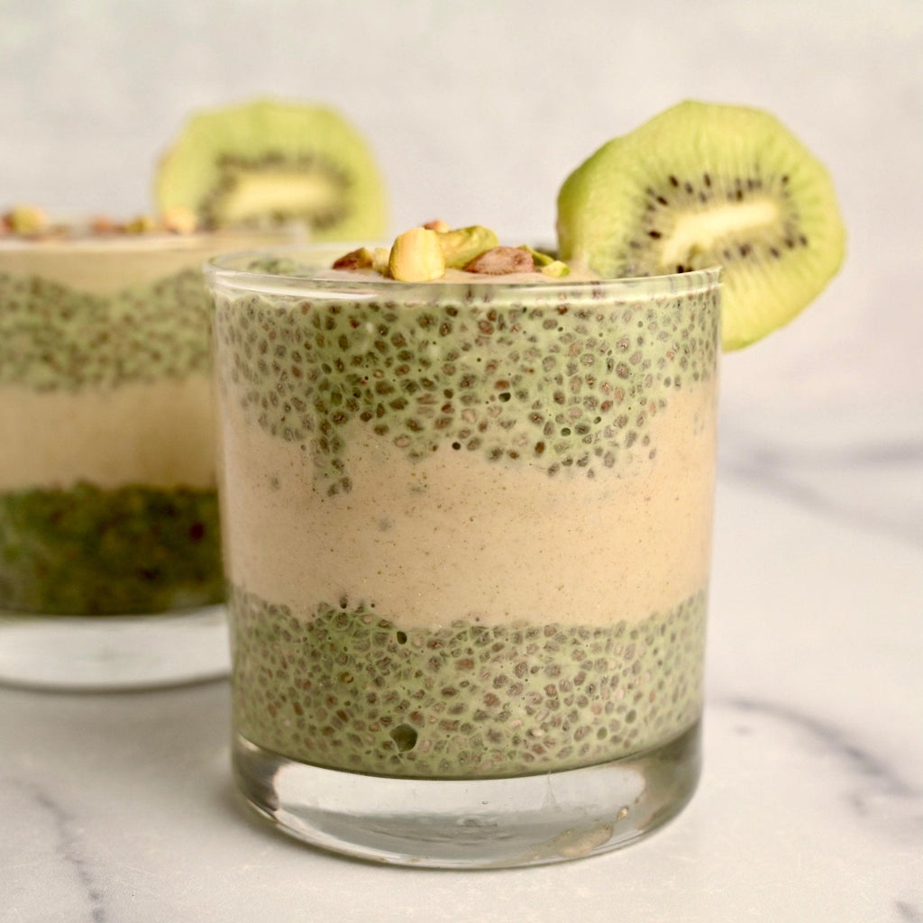 A glass cup filled with green chia seed pudding with a fresh slice of kiwi on the rim