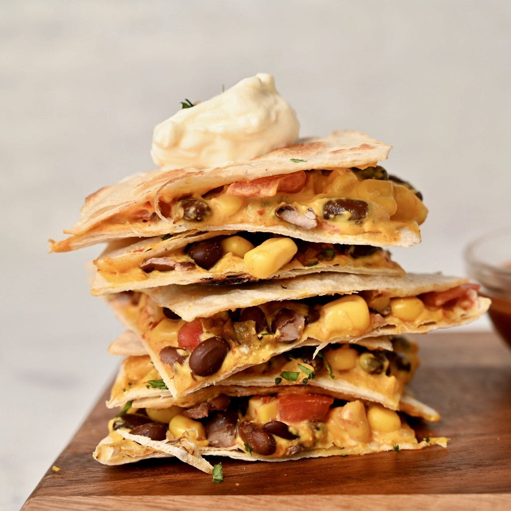 A wooden cutting board stacked with sliced quesadillas