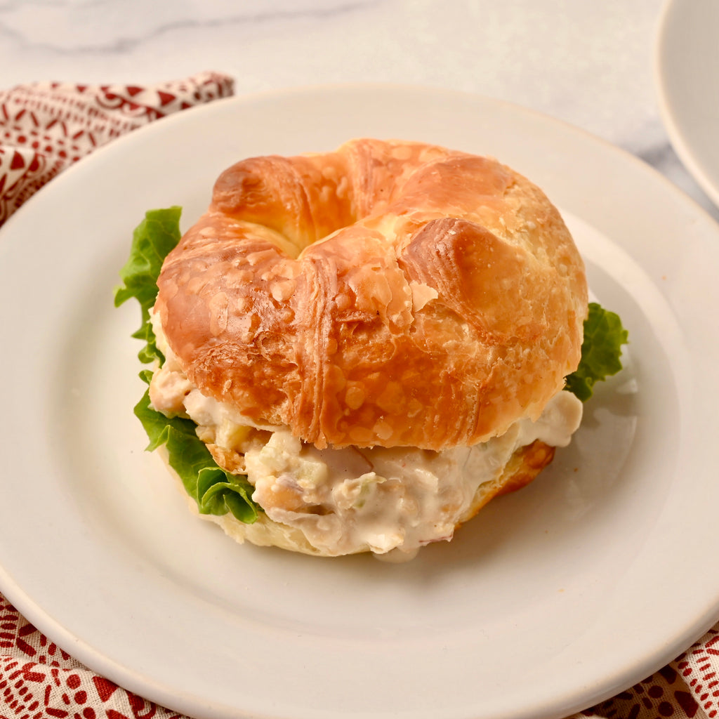 A white plate with a croissant sandwich in the middle of it