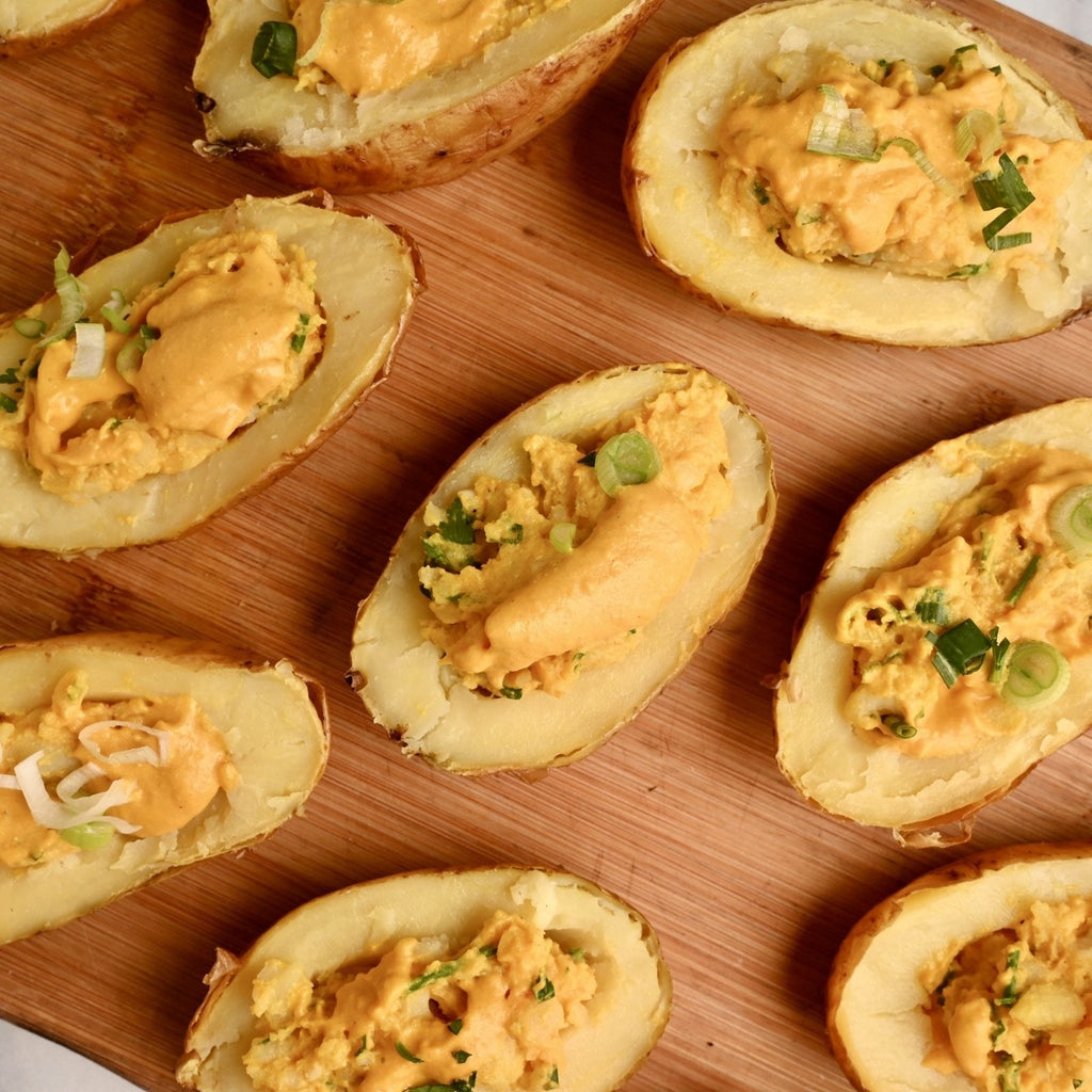 Sliced potato skins filled with a homemade cashew-based filling scattered across a wooden cutting board