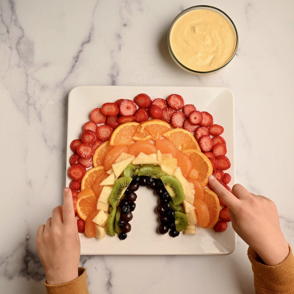 A white square plate with a rainbow made of colorful fresh fruit slices