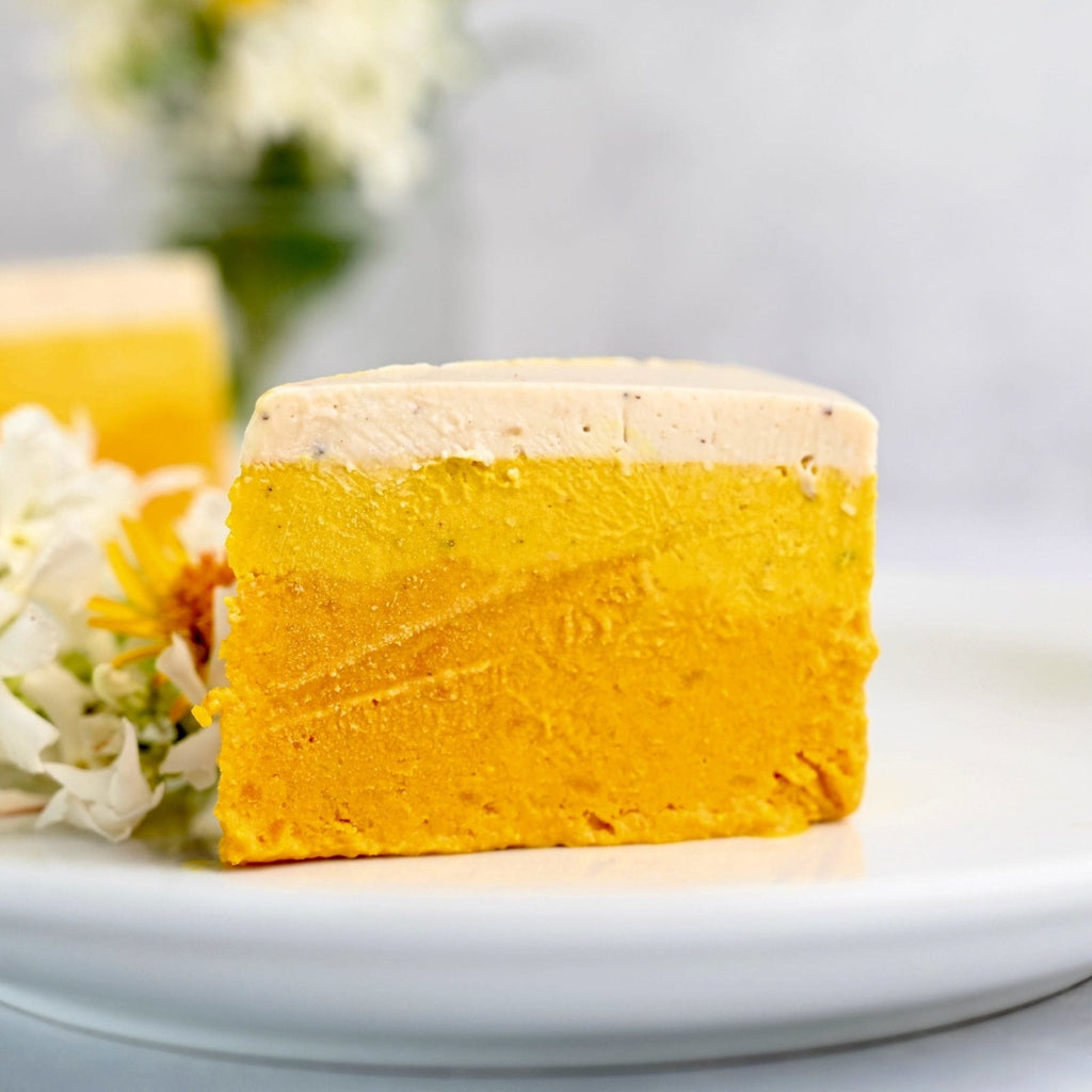 A slice of orange and yellow cheesecake on a white plate with florals off to the side