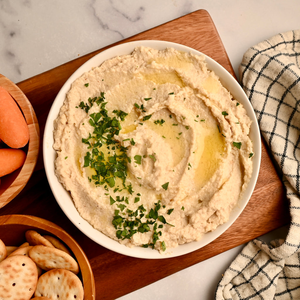 A big bowl of hummus on a wooden cutting board