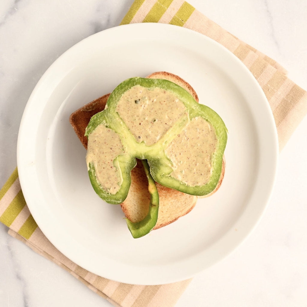 What plate with one slice of toast topped with a slice bell pepper stuffed with an avocado and almond spread
