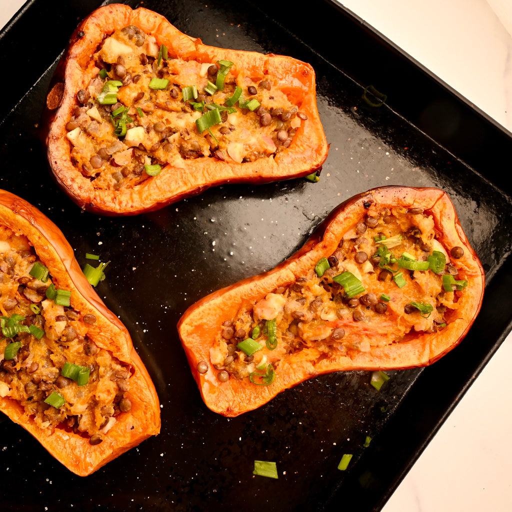 A black cooking tray with roasted stuffed butternut squash halves