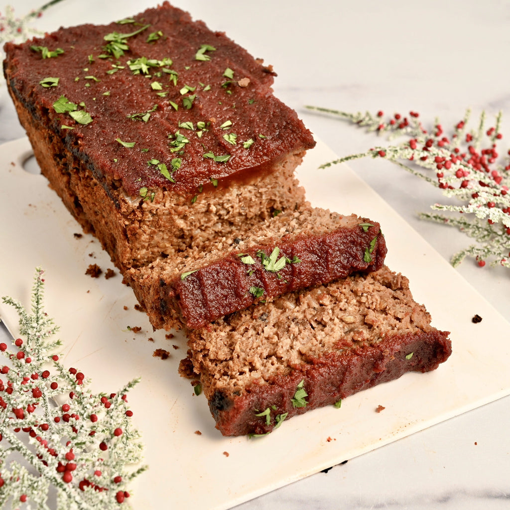 A white serving platter has a homemade nut loaf topped with green herbs on both sides of the white plate are green and red plant sprigs