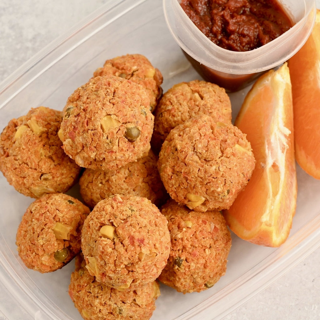 A clear container filled with an array of small orange veggie balls and a dipping sauce