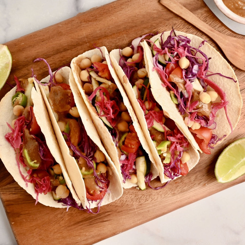 Wood cutting board with four soft shelled tacos filled with fresh vegetables