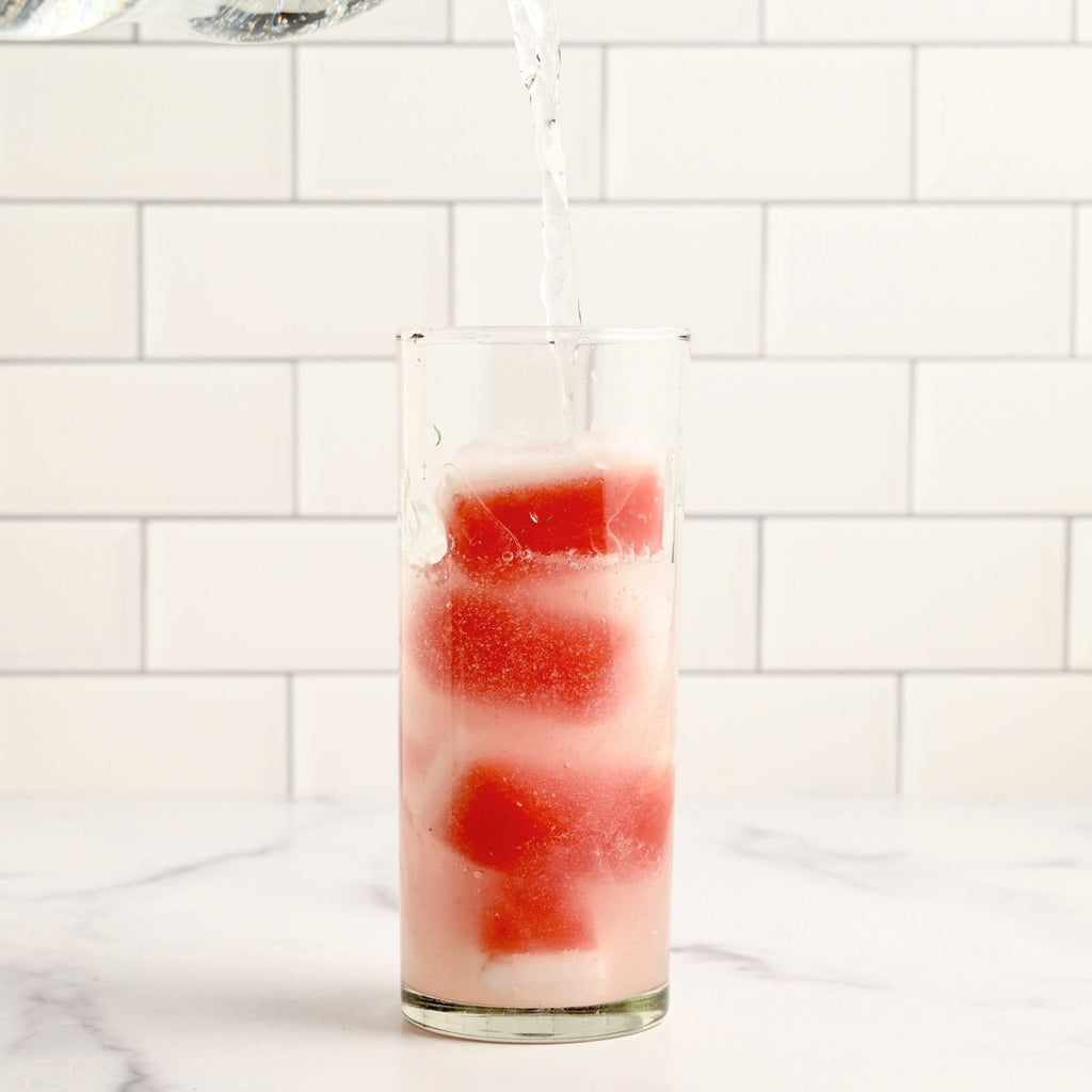One clear glass filled with bright pink watermelon coconut ice cubes