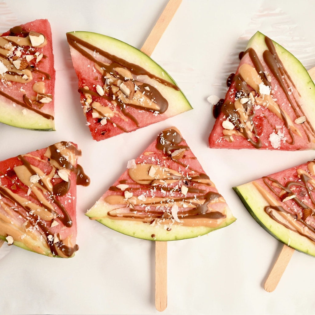 Slices of watermelon drizzled with chocolate sauce and poked through with wooden popsicle sticks