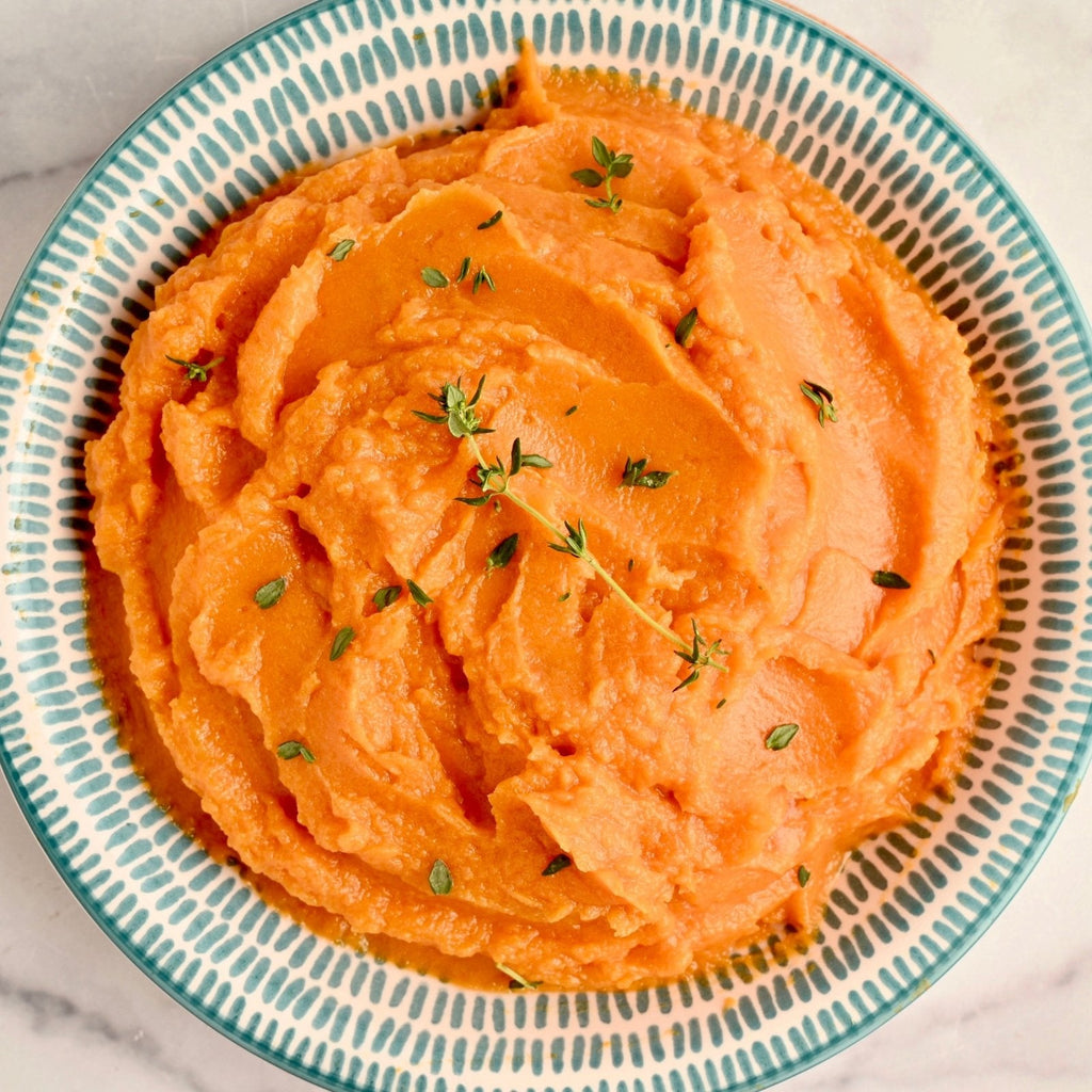 A big ceramic bowl filled with creamy mashed sweet potatoes