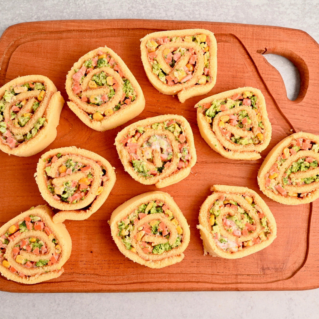 Wooden cutting board is covered in bite sized plant based veggie pinwheels
