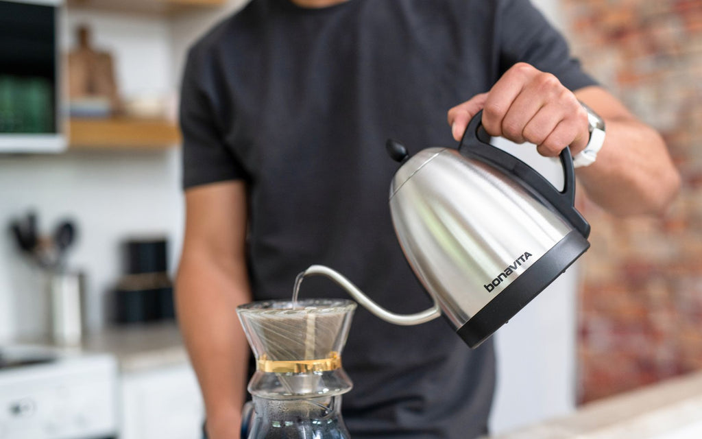 Man is pouring hot water from a variable temperature kettle into a coffee dripper.