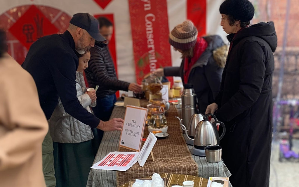 Several individuals in winter coats are being served tea at an outdoor event.