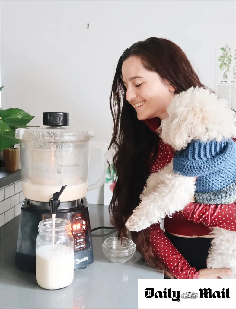 Woman holding poodle dog checking on her oat milk as it pours into a jar.